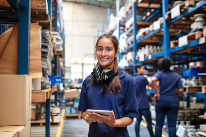 A girl standing in a fulfillment centre warehouse holding inventory sheet and smiling